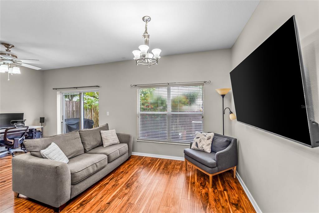 A living room features wood flooring, a gray sofa, an armchair, and a wall-mounted television — 11014 BLAINE TOP PLACE, TAMPA, FL