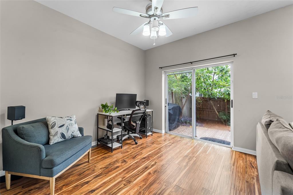 A living room with wood-look flooring, a blue sofa, a computer desk, and sliding glass doors — 11014 BLAINE TOP PLACE, TAMPA, FL