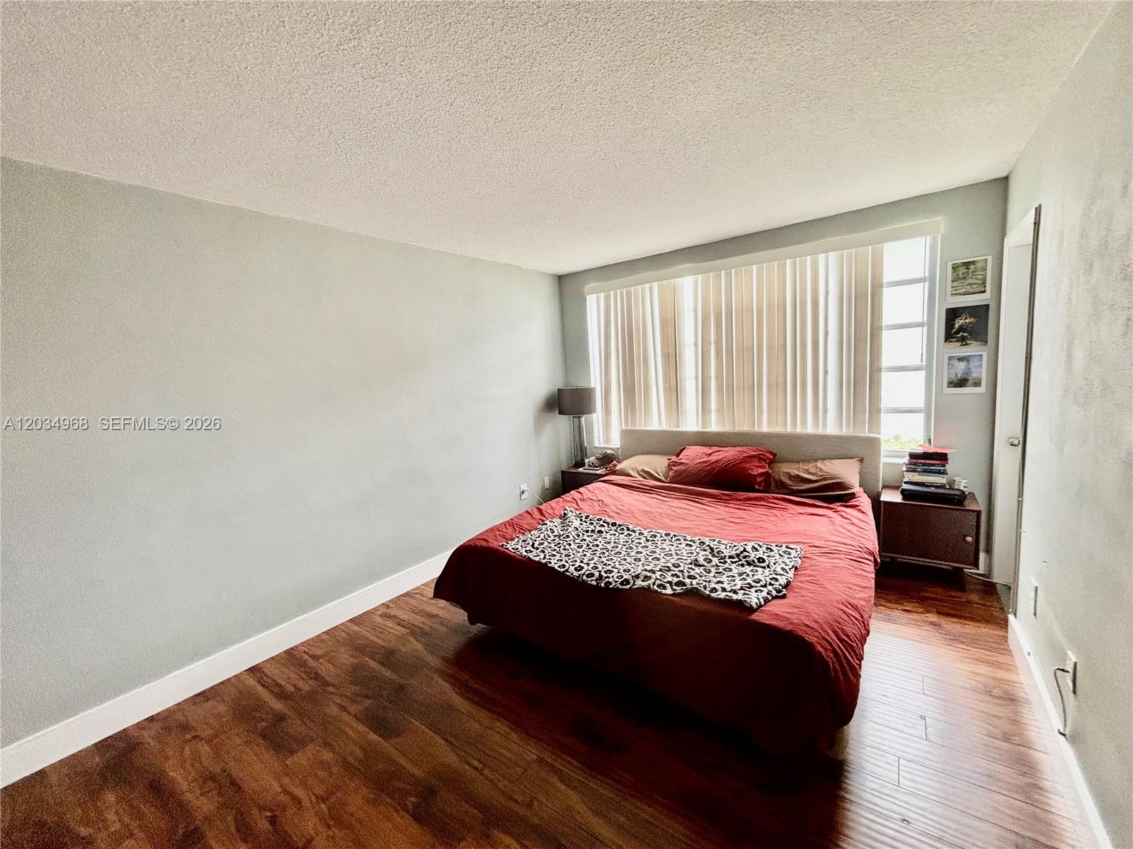 A bedroom features a red bed, wood flooring, and a large window with vertical blinds — 1304 NE 191st St # A232, Miami FL 33179, MIAMI, FL