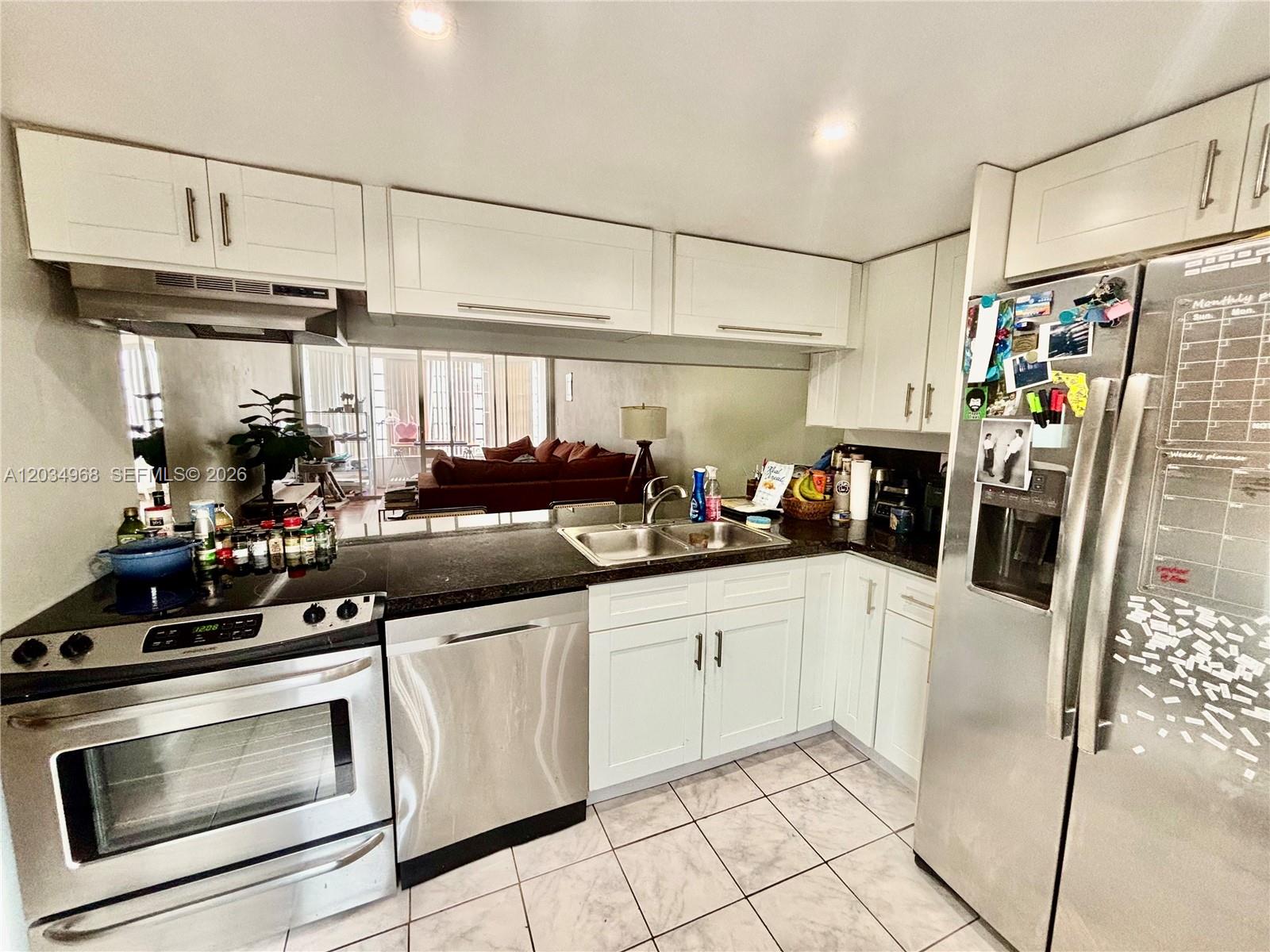 A kitchen features white cabinets, stainless steel appliances, a dark countertop, and a mirrored backsplash — 1304 NE 191st St # A232, Miami FL 33179, MIAMI, FL