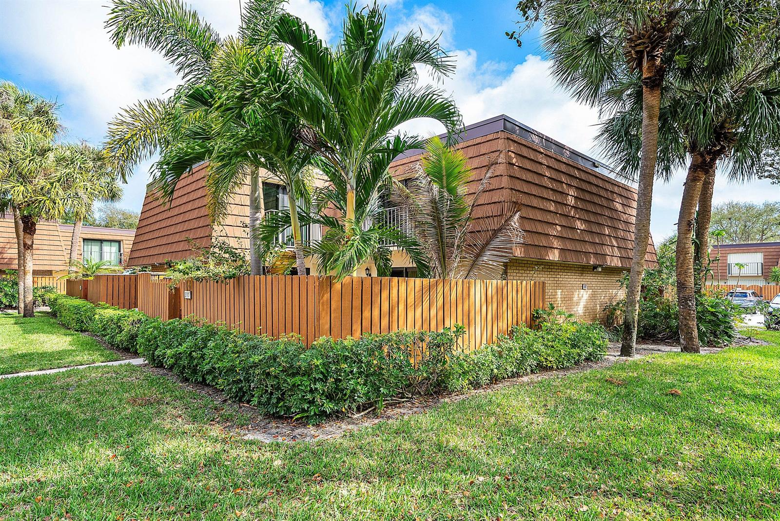 A two-story building with a mansard roof stands behind a wooden fence and palm trees — 2715 27th Court, Jupiter FL 33477, JUPITER, FL