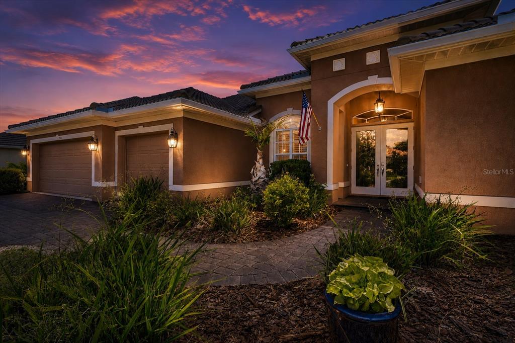 A single-story house exterior with a paved walkway, garage, and an American flag at dusk — 315 PETREL TRAIL, BRADENTON, FL