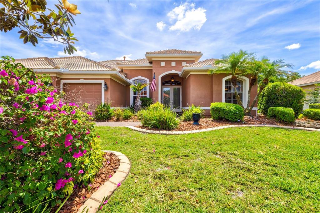A paved walkway leads to the front entrance of a tan stucco home with landscaping — 315 PETREL TRAIL, BRADENTON, FL