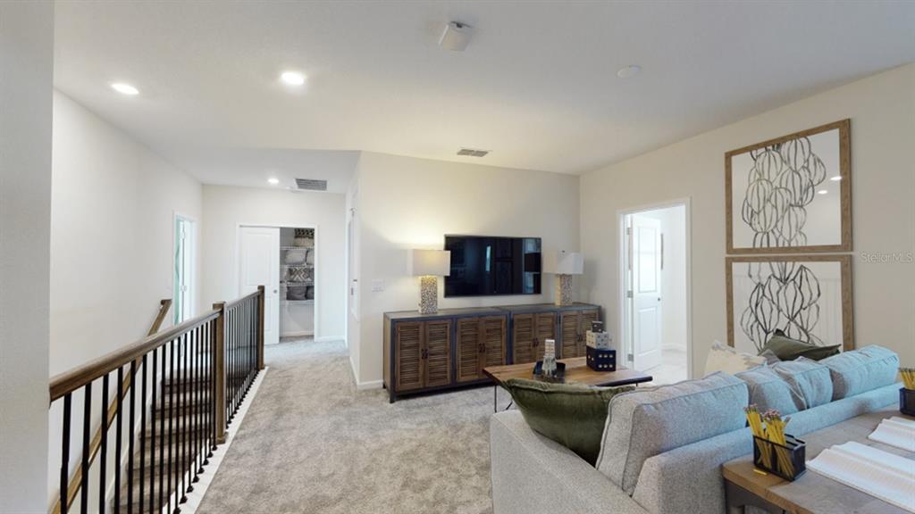 A carpeted loft area features a television console, a sofa, and a staircase railing — 5620 FIONA LANE, ST CLOUD, FL