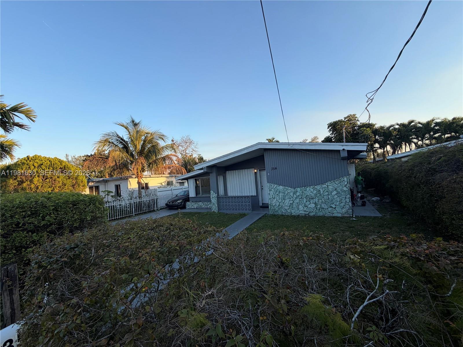 A single-story gray house with stone accents and a palm tree in the front yard — 354 NE 173rd St, North Miami Beach FL 33162, NORTH MIAMI BEACH, FL
