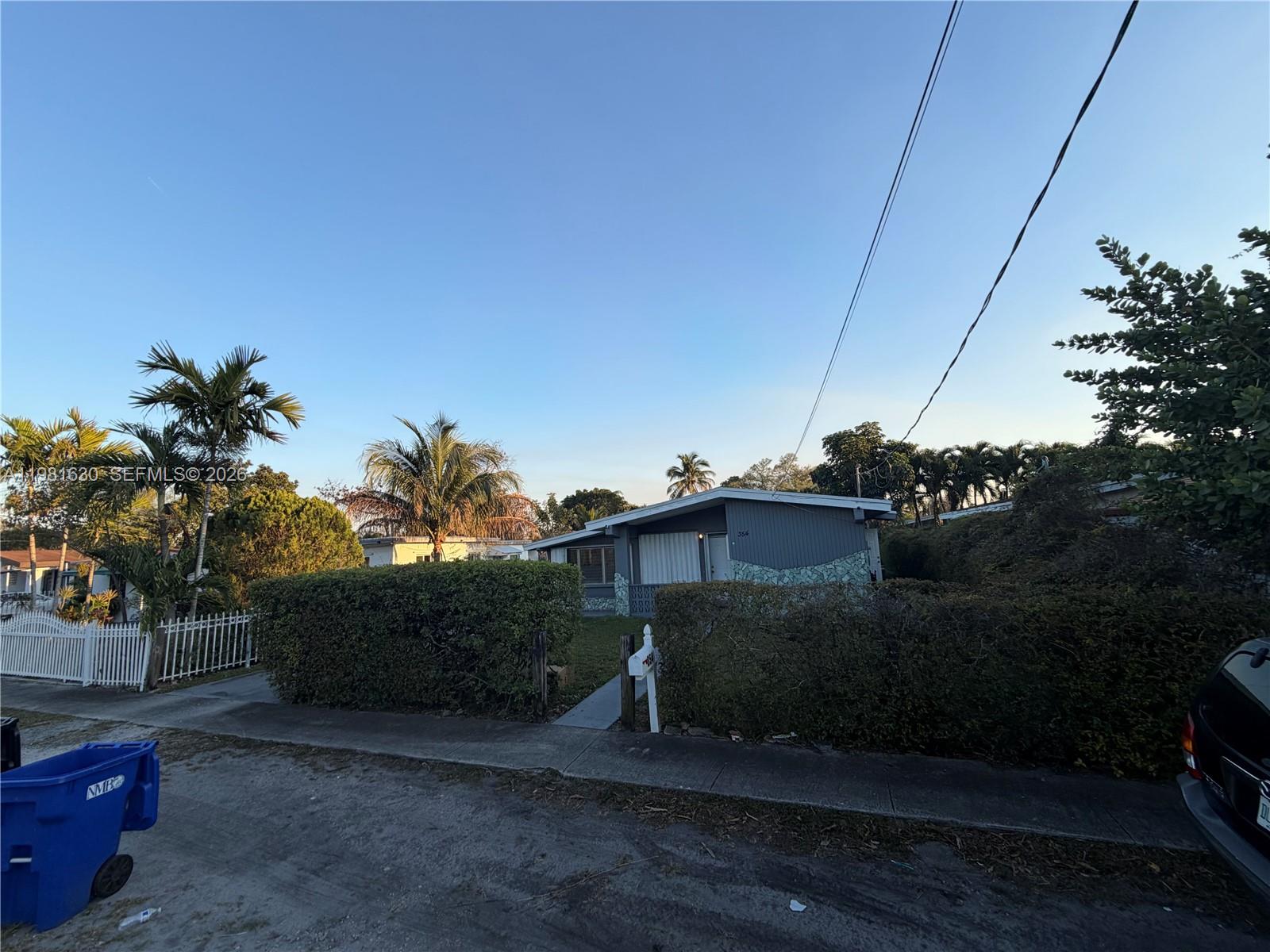 A single-story house with gray siding and stone accents sits behind a tall hedge — 354 NE 173rd St, North Miami Beach FL 33162, NORTH MIAMI BEACH, FL
