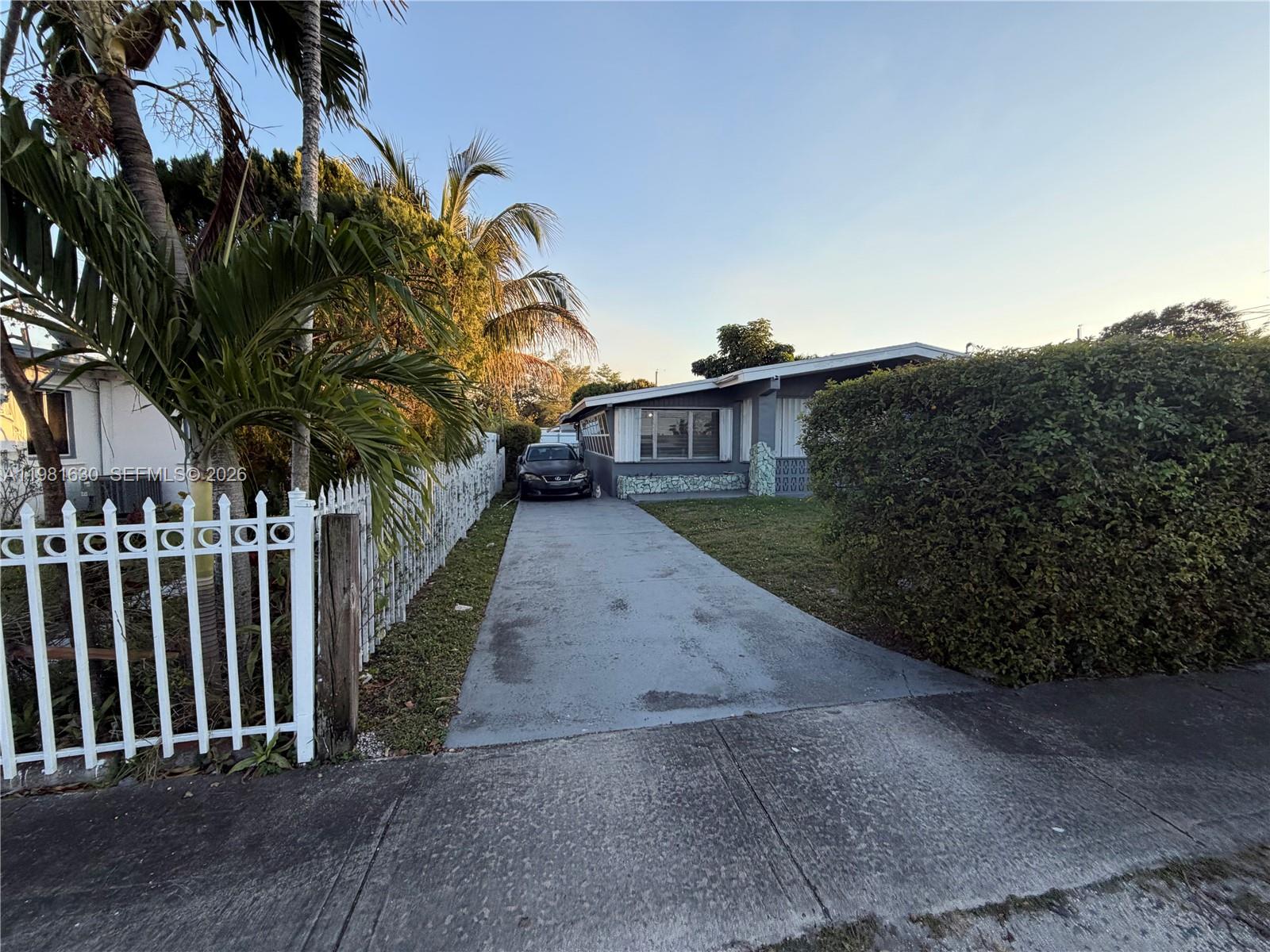 A gray house with a concrete driveway and a white fence sits behind a hedge — 354 NE 173rd St, North Miami Beach FL 33162, NORTH MIAMI BEACH, FL