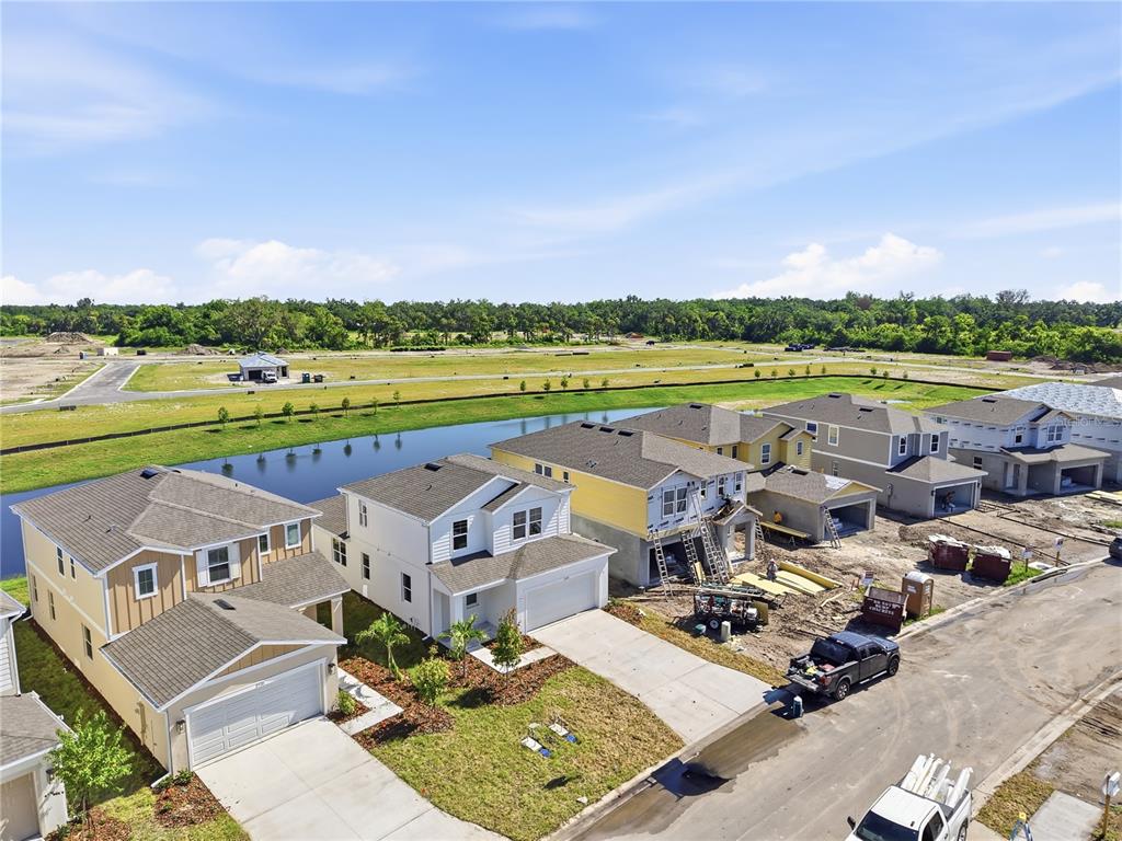An aerial view shows several newly constructed suburban houses near a pond and undeveloped land — 2524 29TH LANE E, PALMETTO, FL