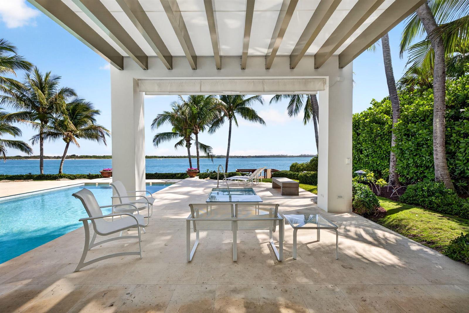 A covered patio with white metal furniture overlooks a swimming pool and the ocean — 7034 SE Harbor Circle, Stuart FL 34996, STUART, FL