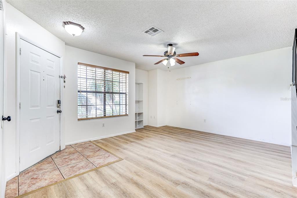 An empty living room features light wood-look flooring, a ceiling fan, and a front door — 2901 WAREHAM COURT, CASSELBERRY, FL
