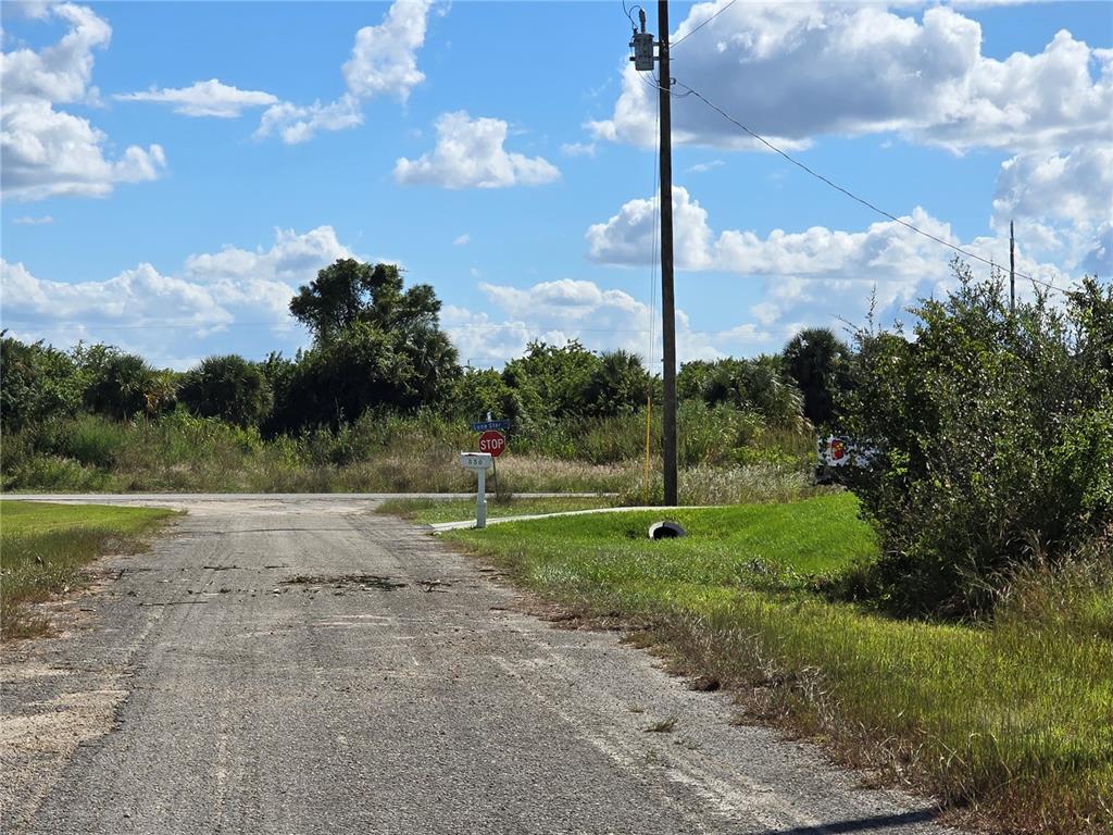 A gravel driveway leads to a stop sign at a rural intersection under a blue sky — 526 CABLE AVENUE S, LEHIGH ACRES, FL