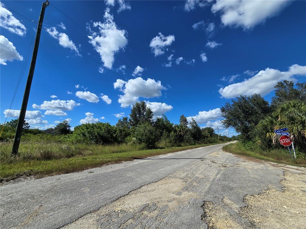 A paved road leads toward a stop sign at a rural intersection under a blue sky — 526 CABLE AVENUE S, LEHIGH ACRES, FL