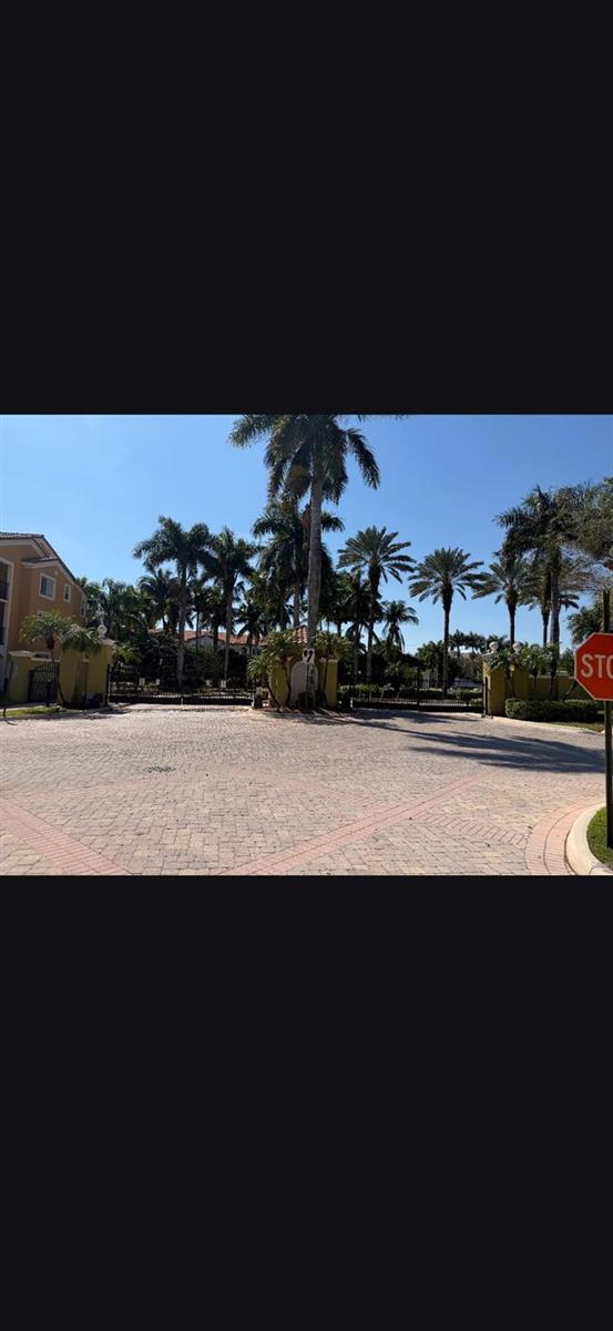 A paved entrance with palm trees leads to a gated community gatehouse under a blue sky — 2090 W Preserve Way # 206, Miramar FL 33025, MIRAMAR, FL