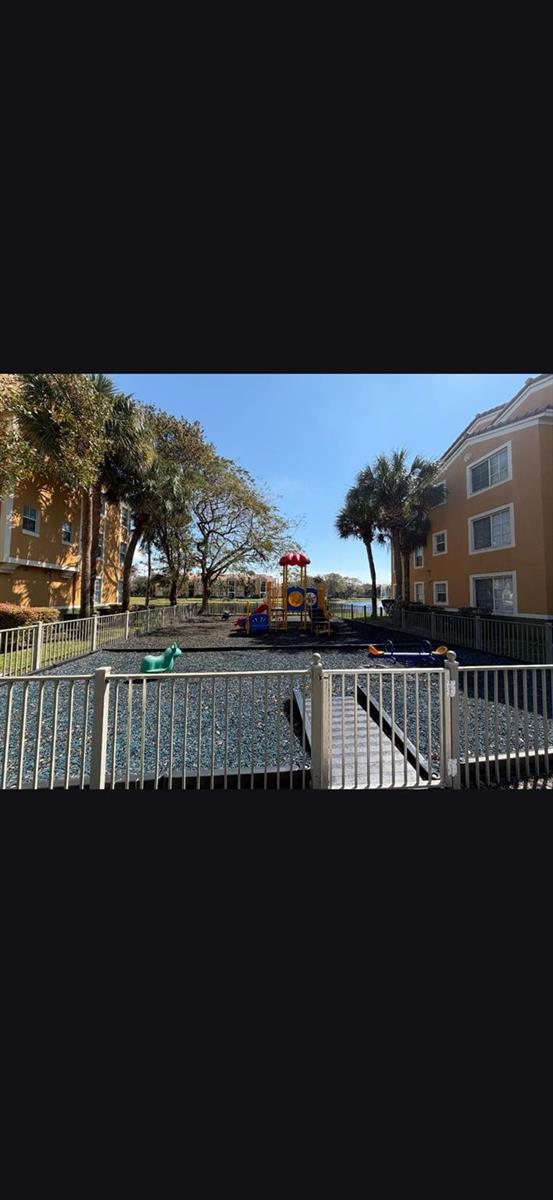 A fenced-in playground with a play structure sits between two multi-story apartment buildings — 2090 W Preserve Way # 206, Miramar FL 33025, MIRAMAR, FL