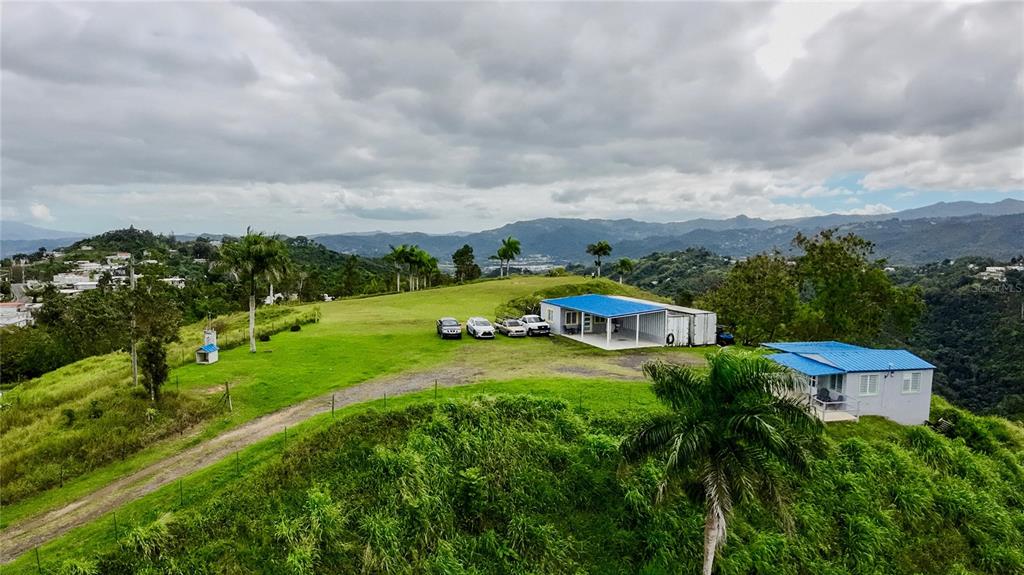 An elevated view shows two small houses with blue roofs on a grassy hillside — 7784 CAÑABONCITO, CAGUAS, PR