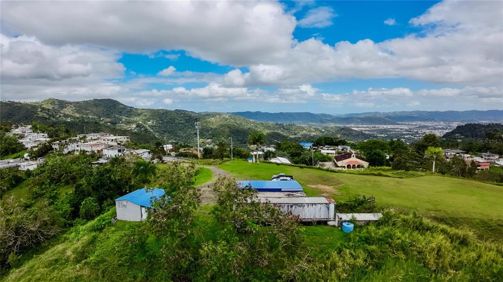 An aerial view shows a grassy hillside with a small house and a storage container — 7784 CAÑABONCITO, CAGUAS, PR