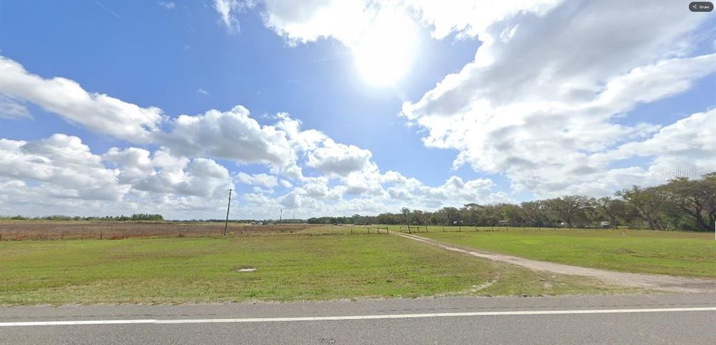 A wide, grassy, undeveloped plot of land sits beside a paved road under a sunny sky — COMMONWEALTH AVE N, POLK CITY, FL
