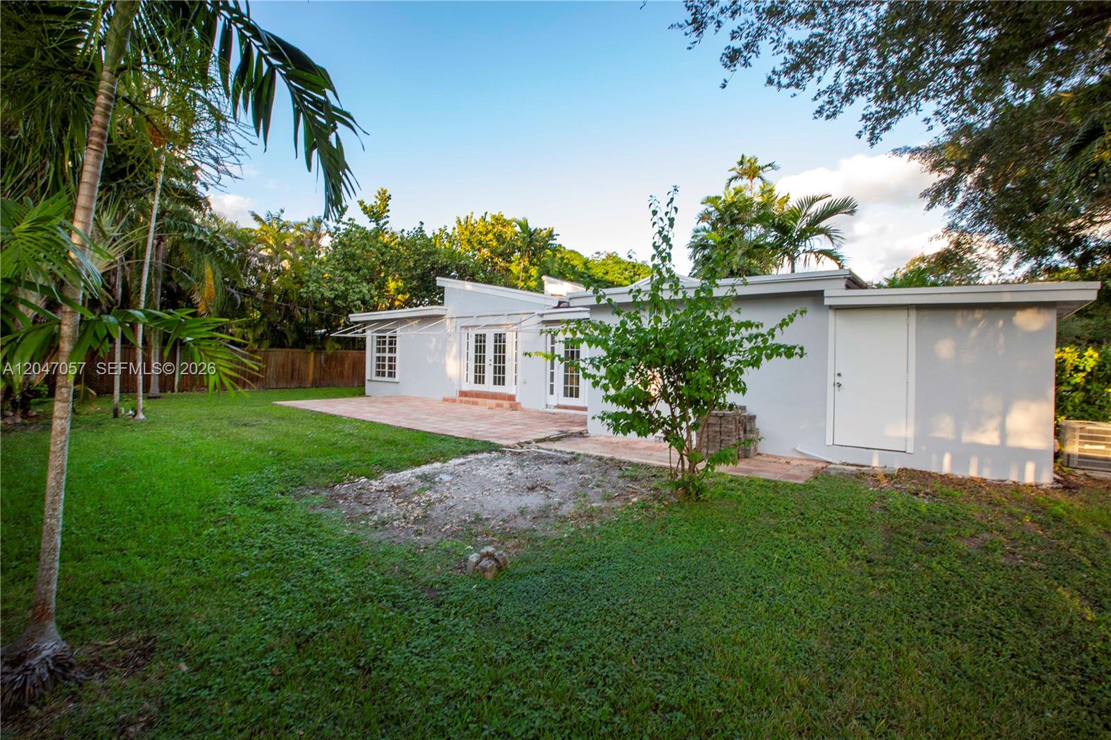 The exterior of a light-colored house features a patio, a grassy yard, and palm trees — 5451 SW 80th St, Miami FL 33143, MIAMI, FL