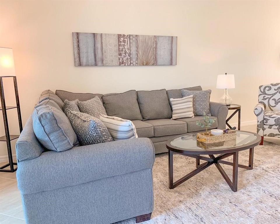 A living room features a grey sectional sofa, a glass-topped coffee table, and wall art — 5710 PALMER CIRCLE UNIT 202, BRADENTON, FL