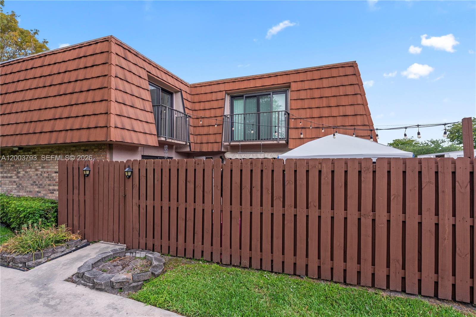 A brown wooden fence encloses a backyard patio area in front of a two-story building — 4089 Forest Hill Dr, Cooper City FL 33026, COOPER CITY, FL