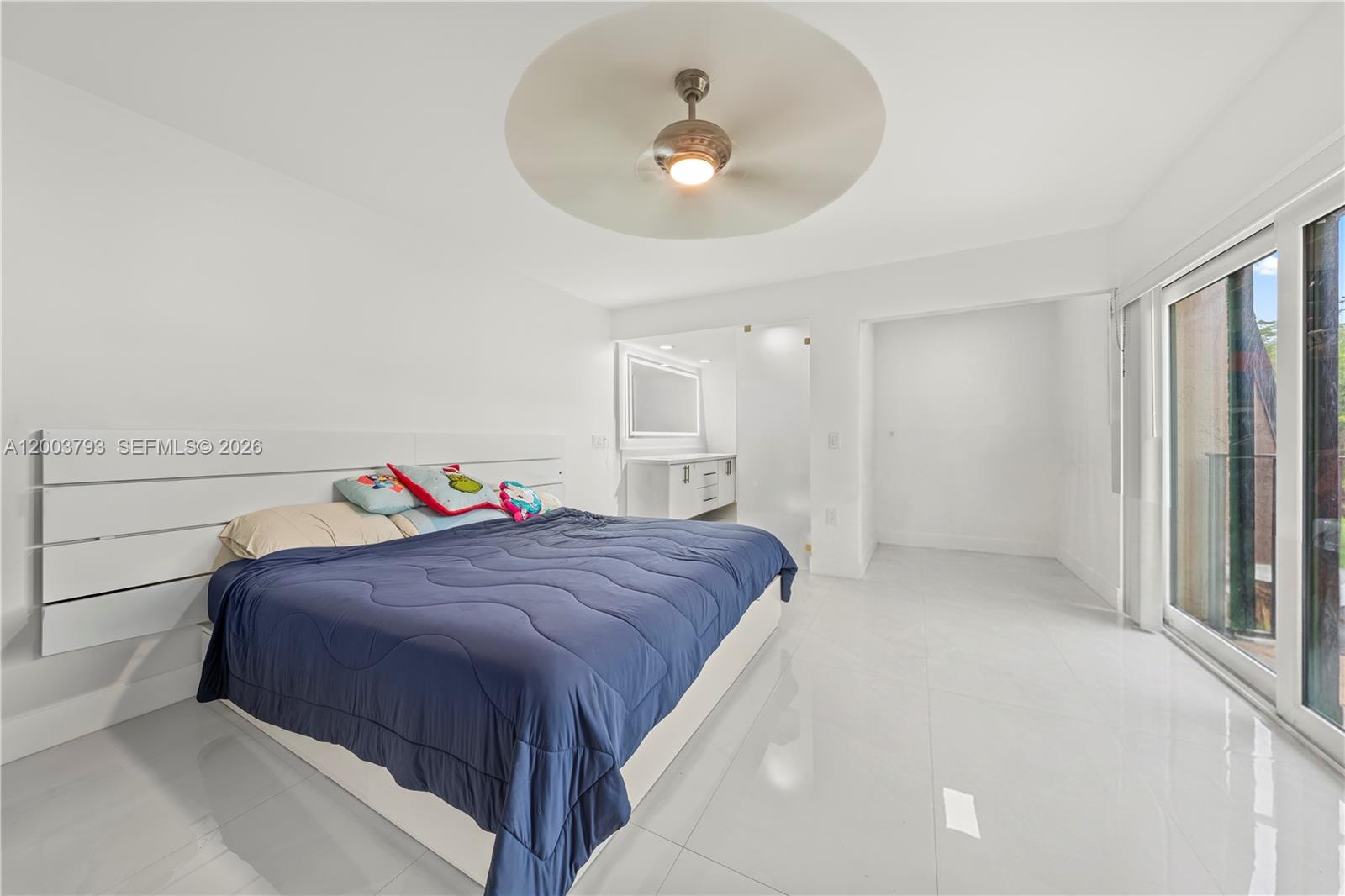 A bedroom features a blue comforter, white platform bed, tiled floors, and a sliding glass door — 4089 Forest Hill Dr, Cooper City FL 33026, COOPER CITY, FL