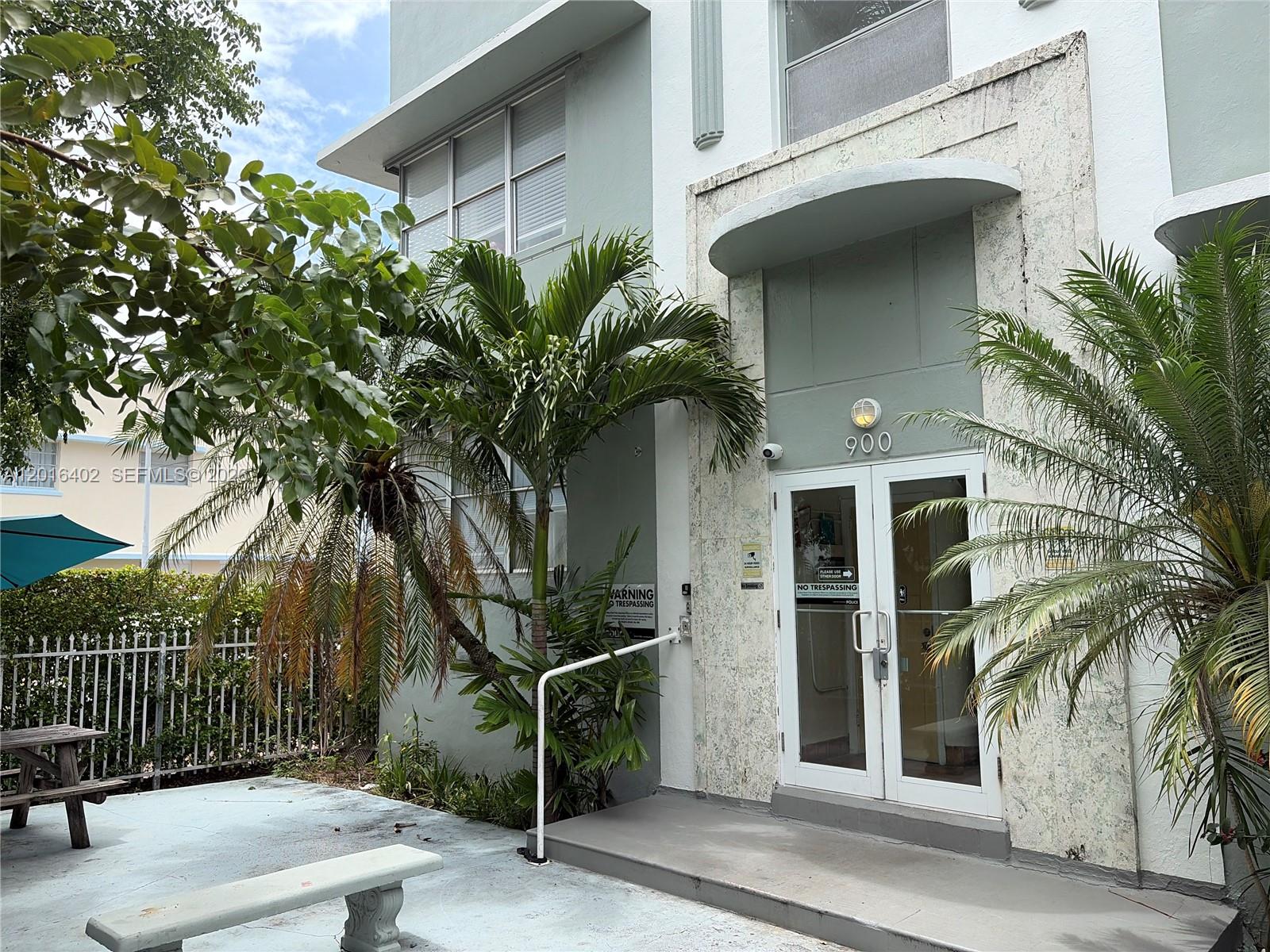 The exterior of a multi-story building features a glass-paned entrance with palm trees and benches — 900 Jefferson Ave # 2, Miami Beach FL 33139, MIAMI BEACH, FL