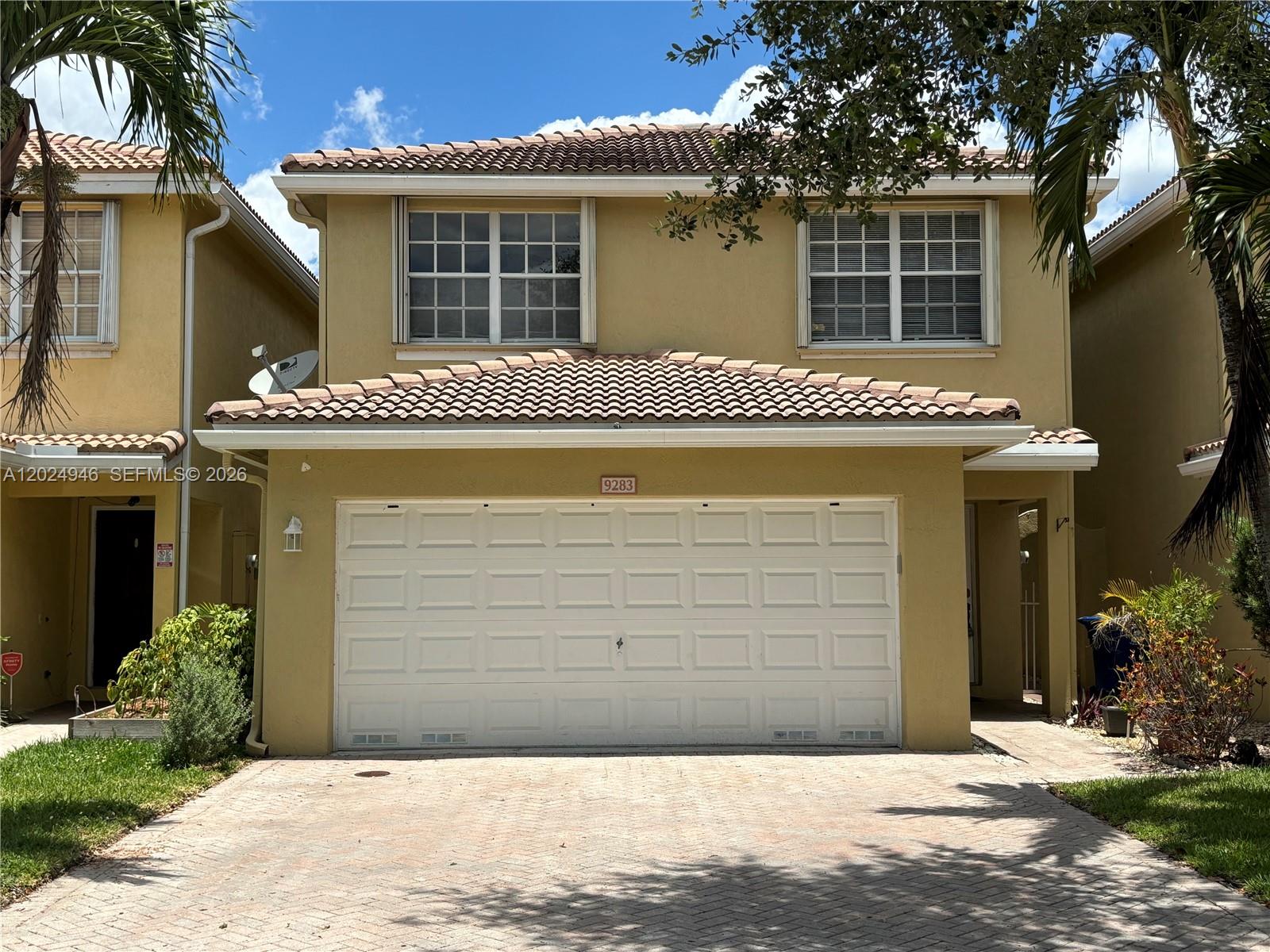 A two-story tan stucco townhouse features a white garage door and a tiled roof — 9283 NW 54th St, Sunrise FL 33351, SUNRISE, FL