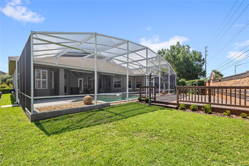 A backyard features a screened-in pool enclosure, a wooden deck, and a grassy lawn — 5713 LIBERTY GARDEN COURT, ORLANDO, FL
