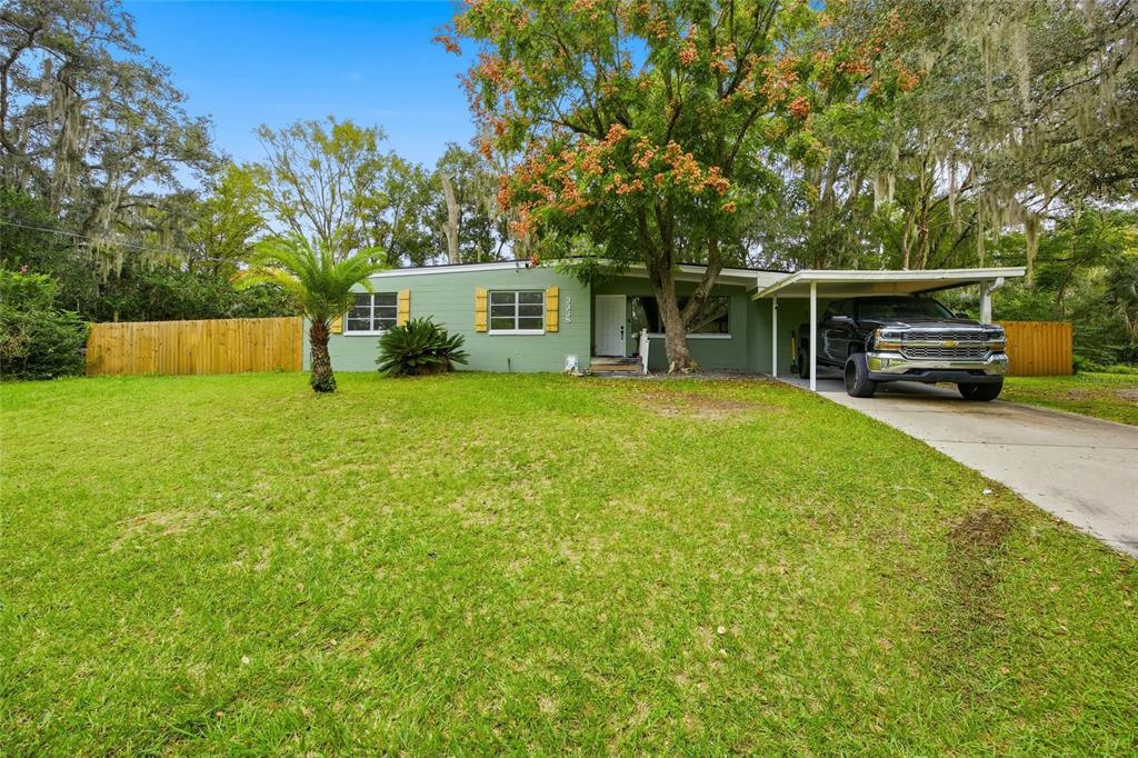 A single-story green house with a carport and a truck parked in the front yard — 3338 SE 6TH STREET, OCALA, FL