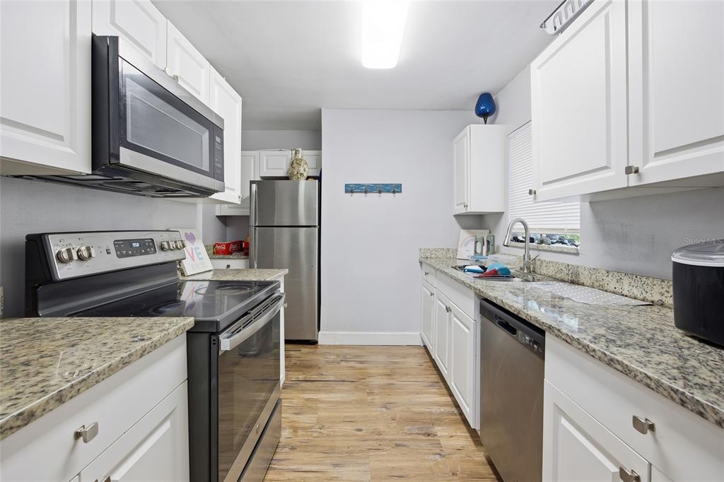 A kitchen features white cabinets, granite countertops, stainless steel appliances, and wood-look flooring — 3338 SE 6TH STREET, OCALA, FL