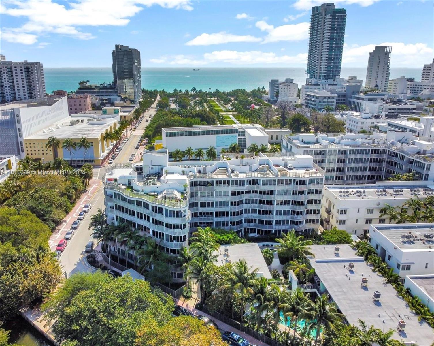 An aerial view shows a multi-story white residential building surrounded by palm trees and city streets — 2155 Washington Ct # 206, Miami Beach FL 33139, MIAMI BEACH, FL