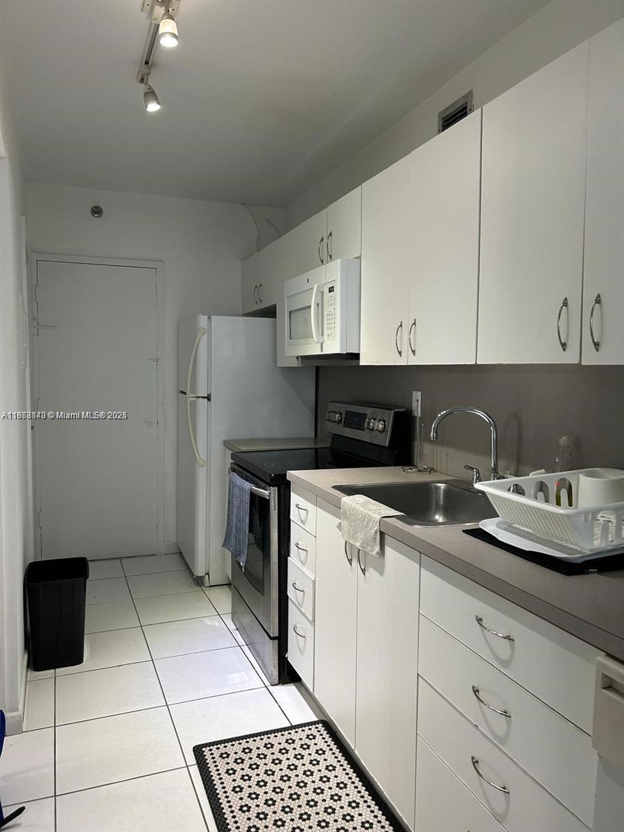 A galley kitchen features white cabinets, stainless steel appliances, and light-colored tile flooring — 100 Lincoln Rd # 437, Miami Beach FL 33139, MIAMI BEACH, FL