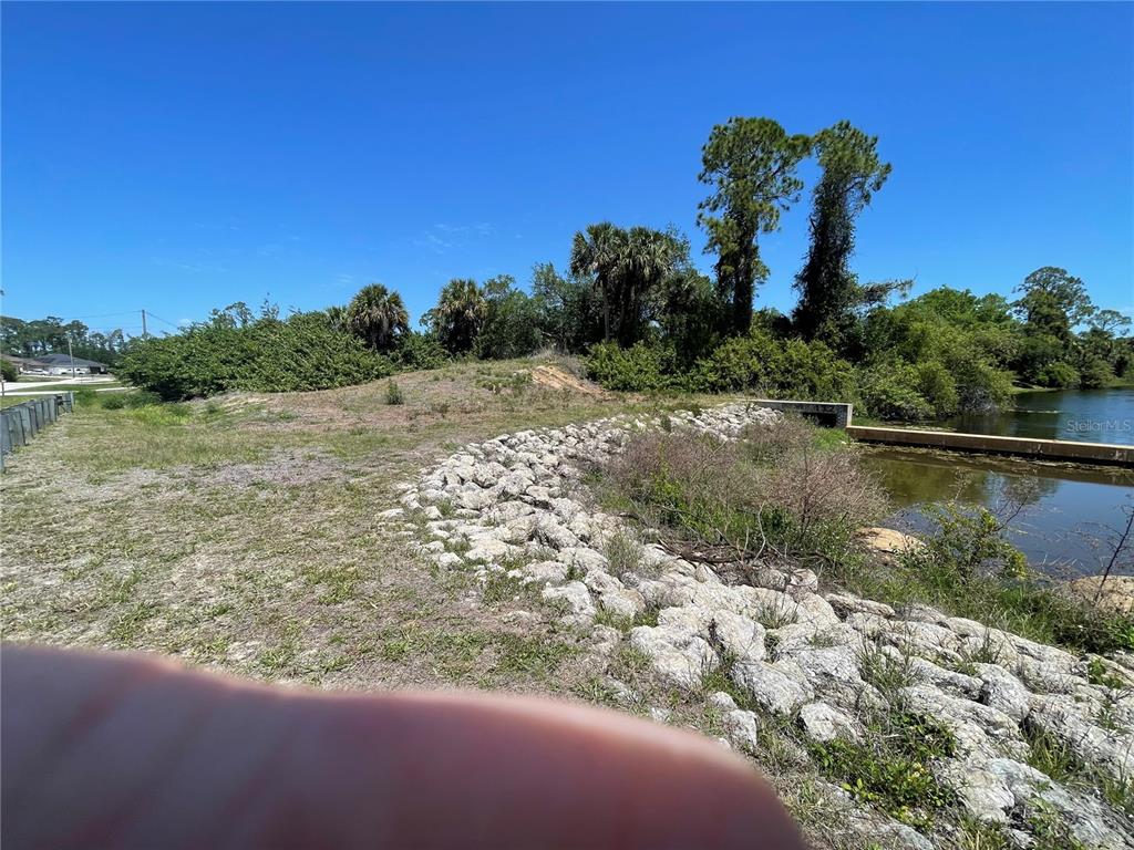A grassy embankment with riprap stone leads to a small pond under a clear sky — Lot#26 JEANNIN DRIVE, NORTH PORT, FL