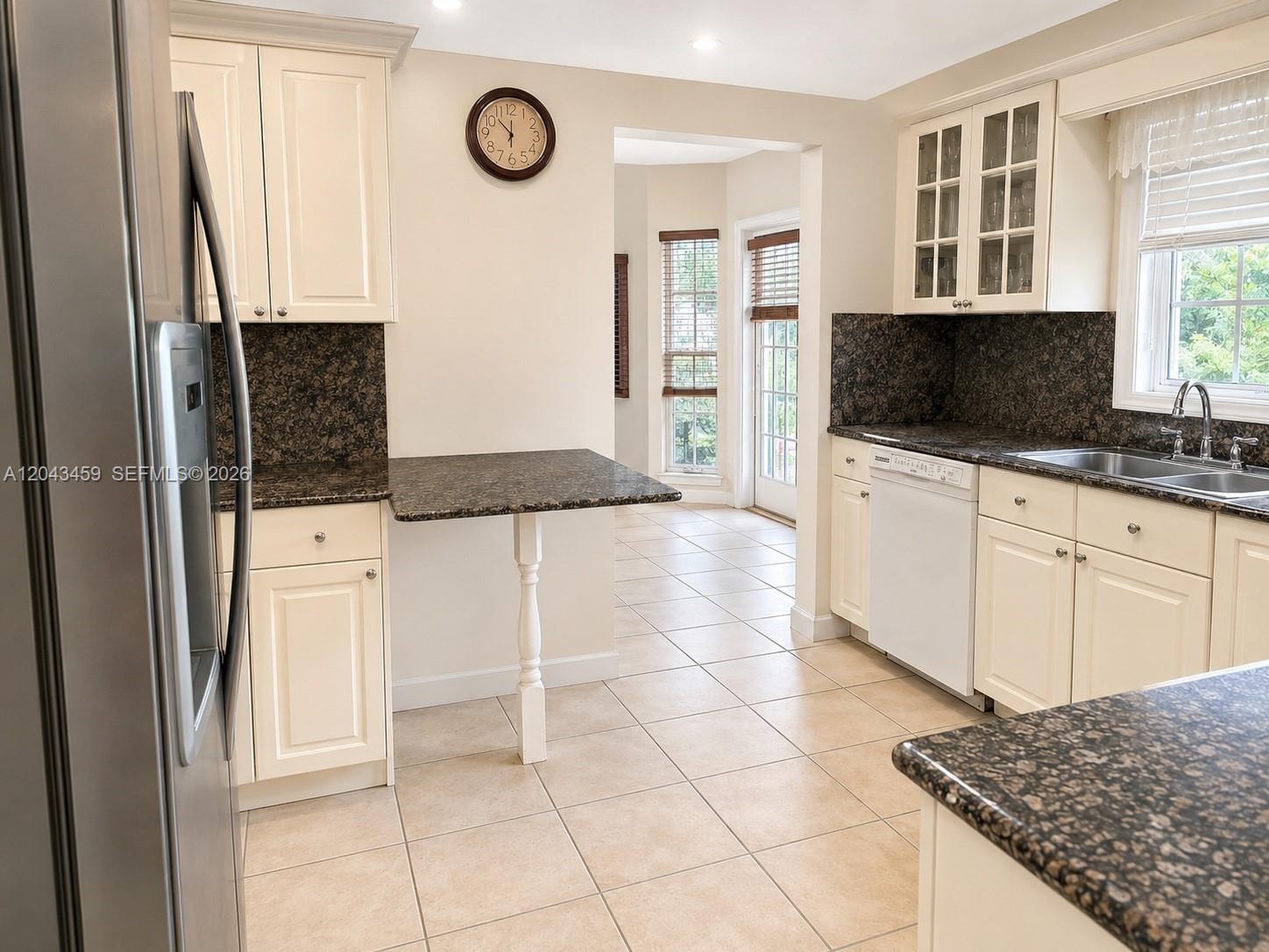 A kitchen features cream-colored cabinets, dark granite countertops, tile flooring, and a small breakfast bar — 9812 SW 77th Pl, Miami FL 33156, MIAMI, FL