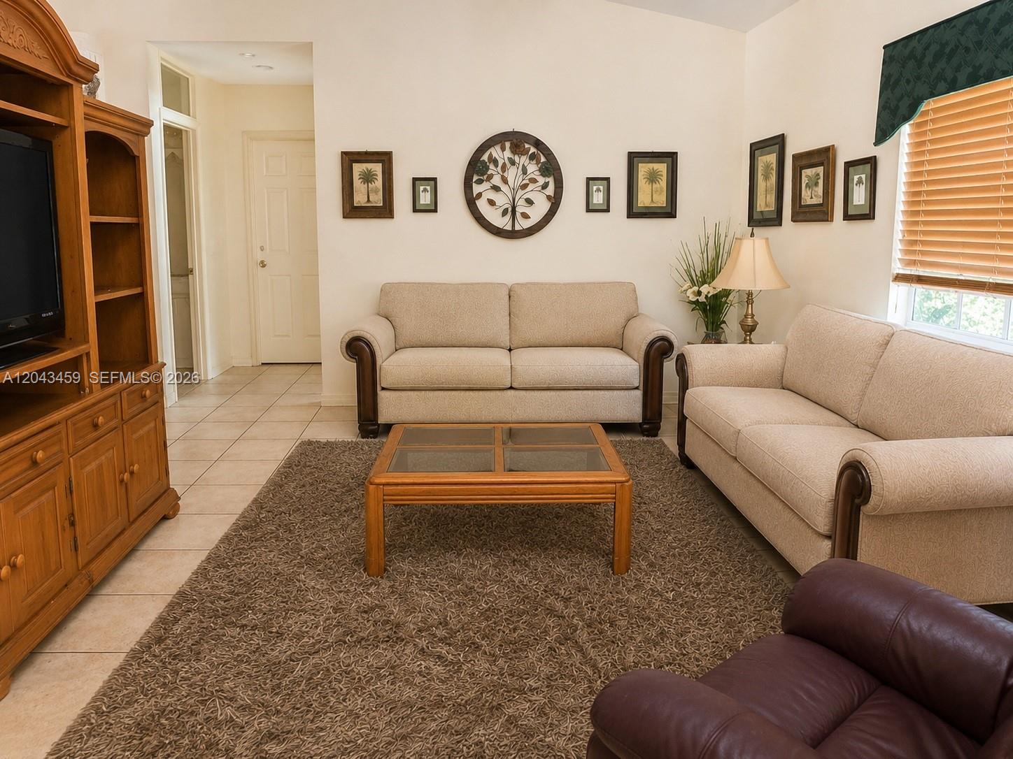 A living room features two beige sofas, a wooden coffee table, and wall-mounted artwork — 9812 SW 77th Pl, Miami FL 33156, MIAMI, FL