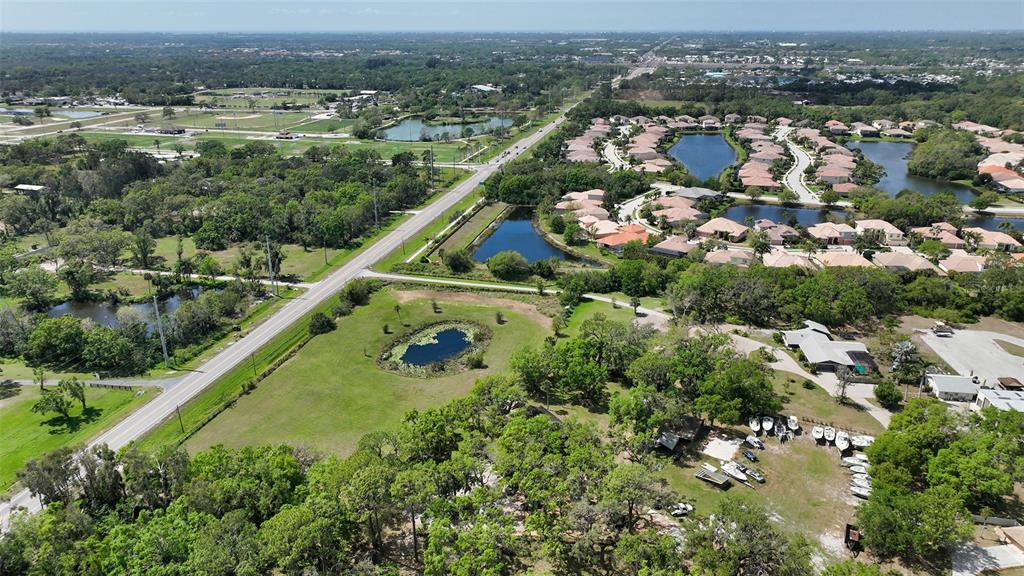 An aerial view shows a road, a small pond, wooded areas, and a residential neighborhood — 7025 CLARK ROAD, SARASOTA, FL