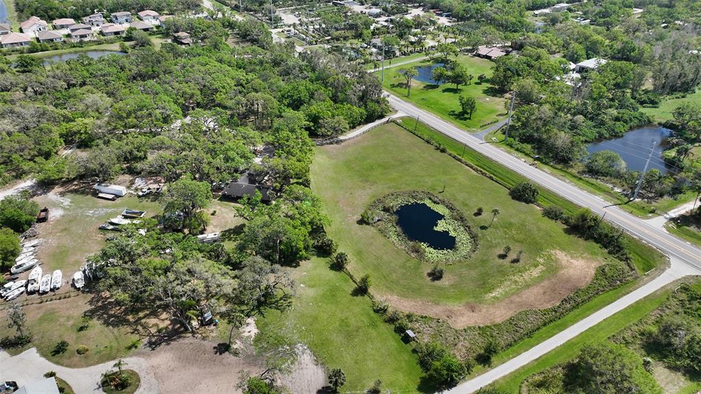 An aerial view shows a grassy lot with a pond, trees, and nearby road — 7025 CLARK ROAD, SARASOTA, FL