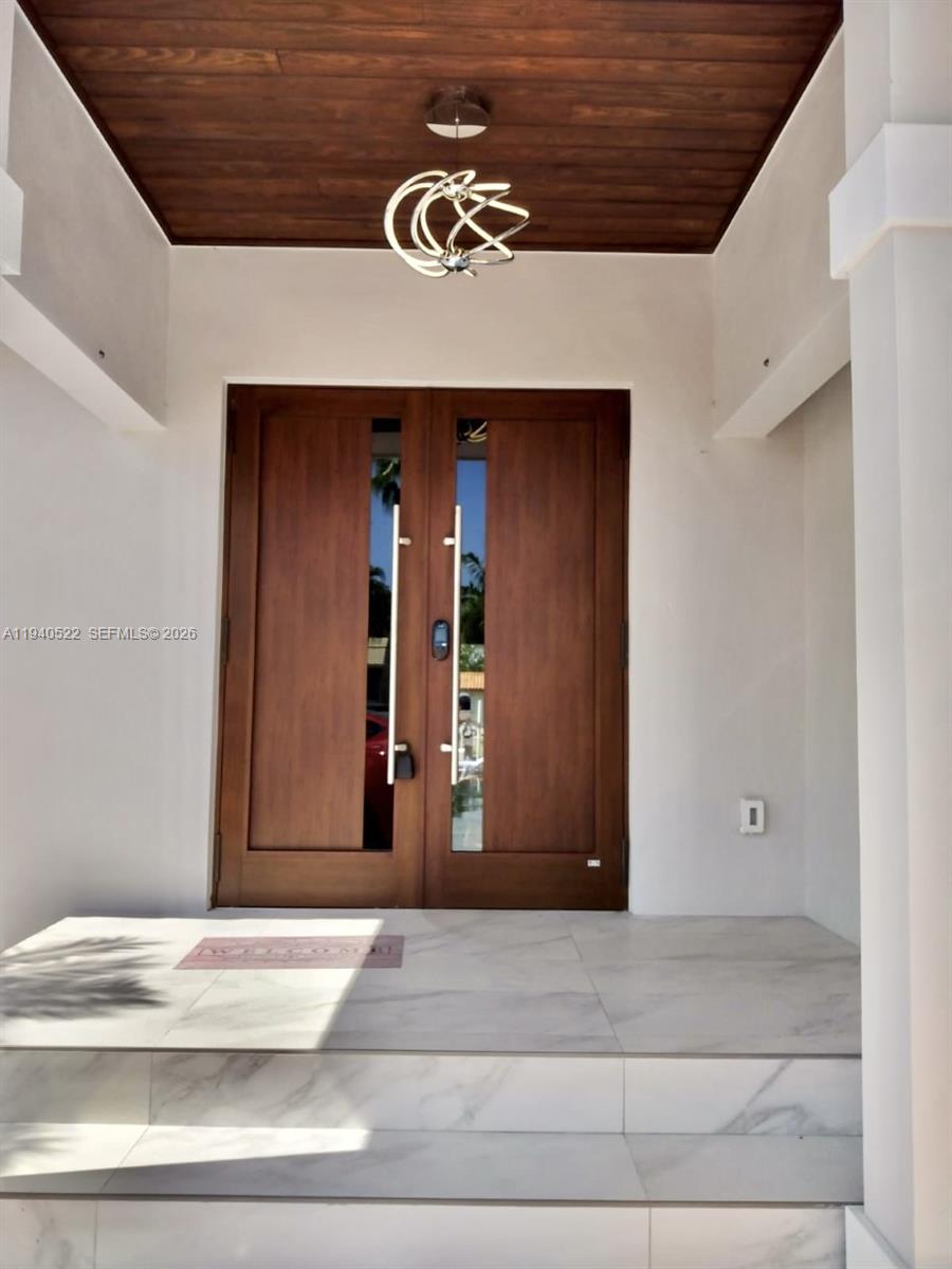 A modern double wooden door with glass panels sits under a wood-paneled porch ceiling — 13240 Ortega Ln, North Miami FL 33181, NORTH MIAMI, FL