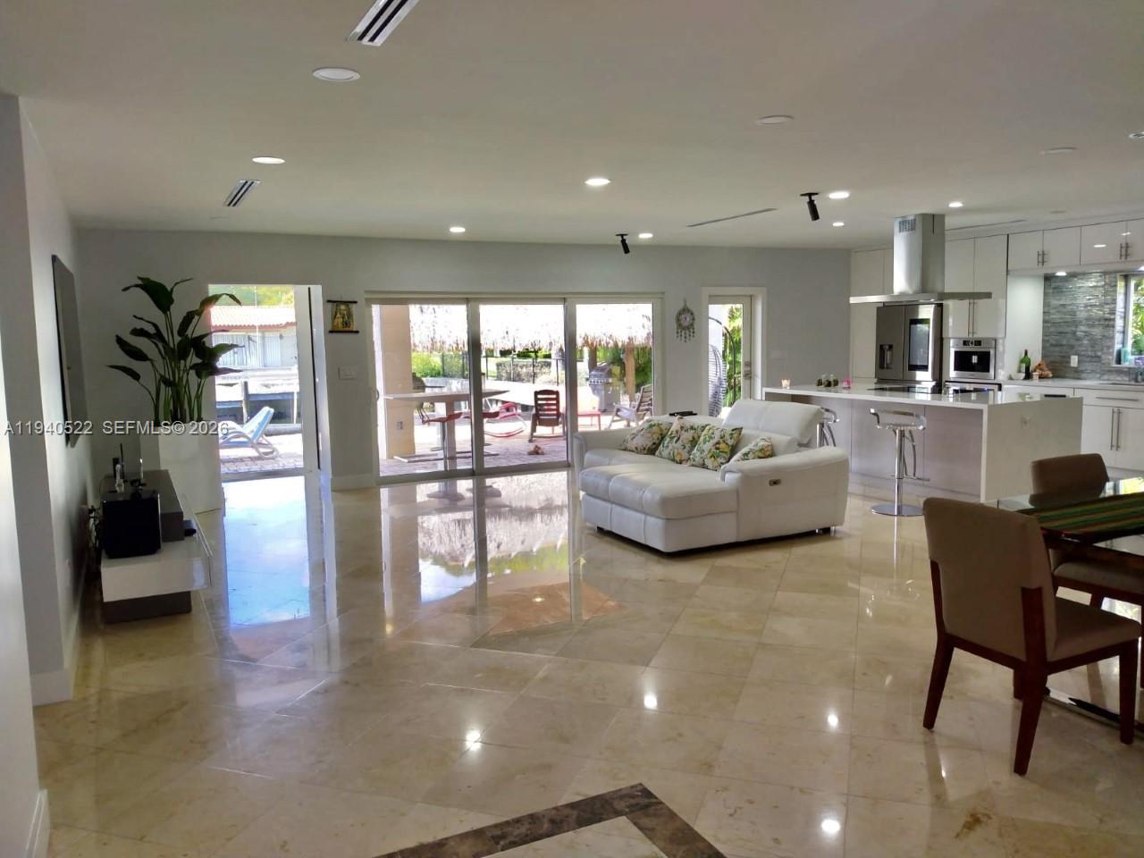 An open-concept living area features a white sofa, kitchen island, and polished tile flooring — 13240 Ortega Ln, North Miami FL 33181, NORTH MIAMI, FL