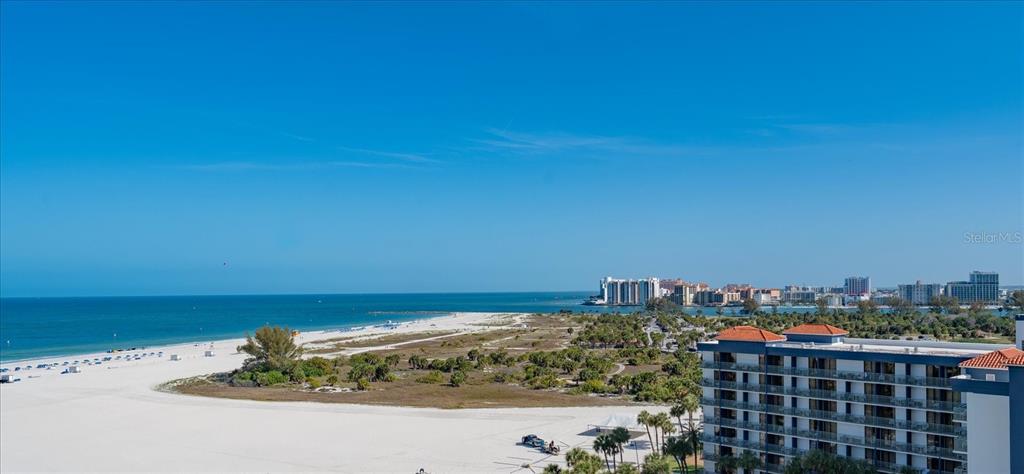 An elevated view of a sandy beach, coastal vegetation, and a multi-story building — 1170 GULF BLVD UNIT 1004, CLEARWATER, FL