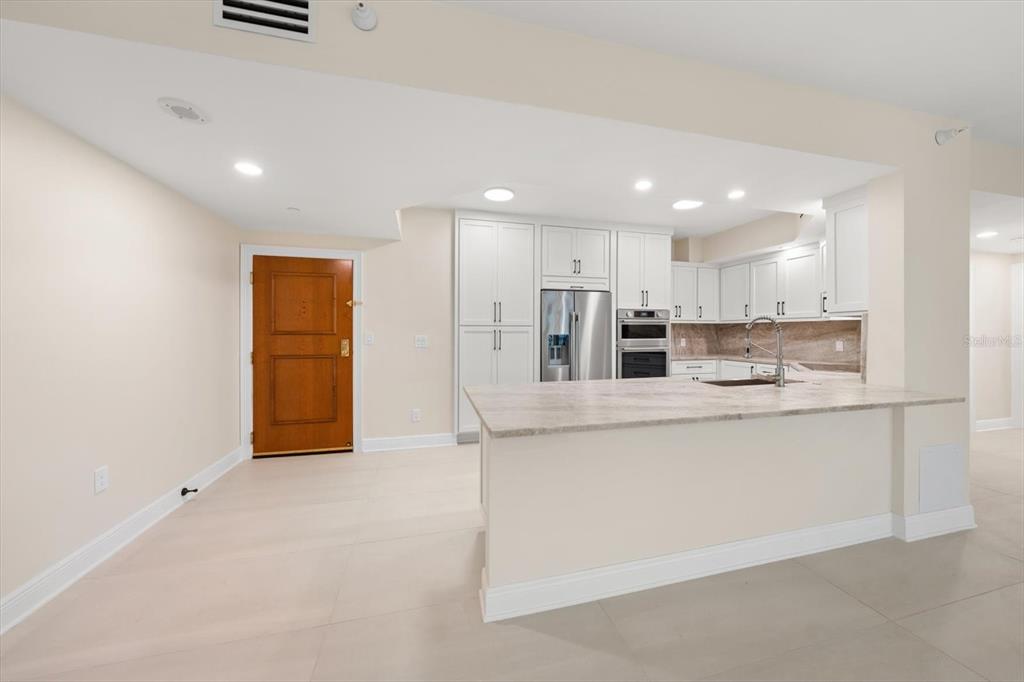 A kitchen features white cabinetry, stainless steel appliances, and a stone-topped island — 1170 GULF BLVD UNIT 1004, CLEARWATER, FL