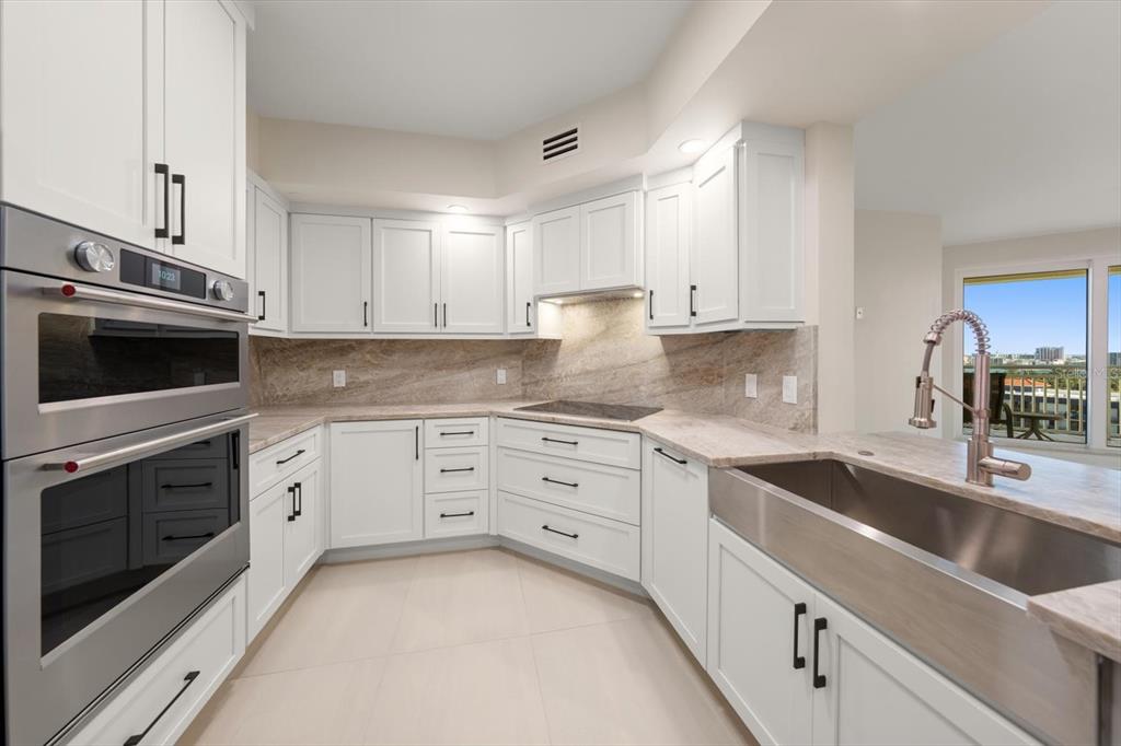 A modern kitchen features white cabinetry, stainless steel appliances, a farmhouse sink, and stone countertops — 1170 GULF BLVD UNIT 1004, CLEARWATER, FL