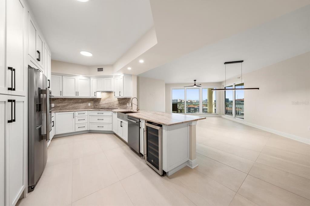 A modern kitchen with white cabinets, stone countertops, and a stainless steel wine cooler — 1170 GULF BLVD UNIT 1004, CLEARWATER, FL