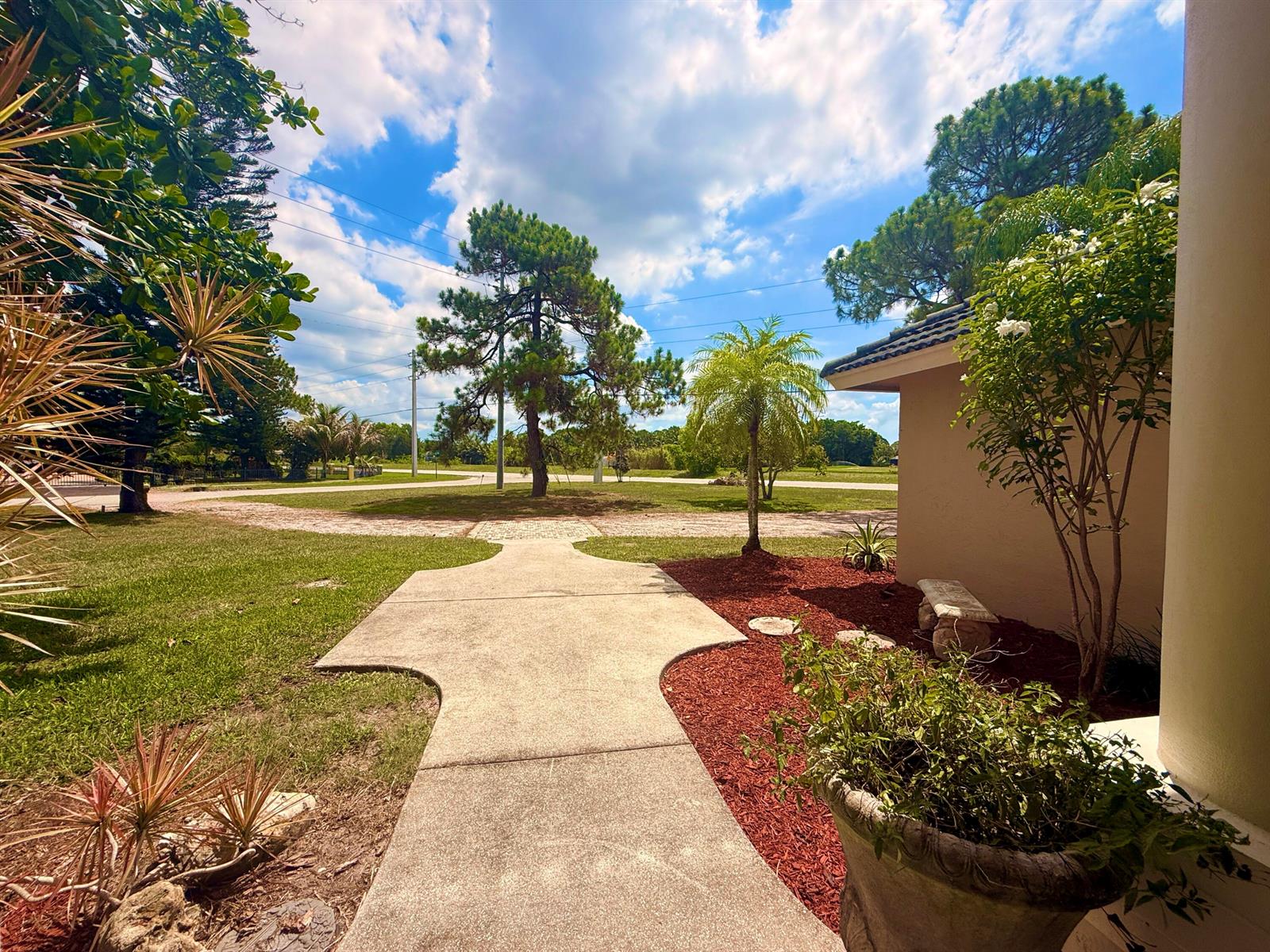 A concrete walkway leads from a house entrance toward a grassy yard with large trees — 12037 Temple Boulevard, FL 33412, FL