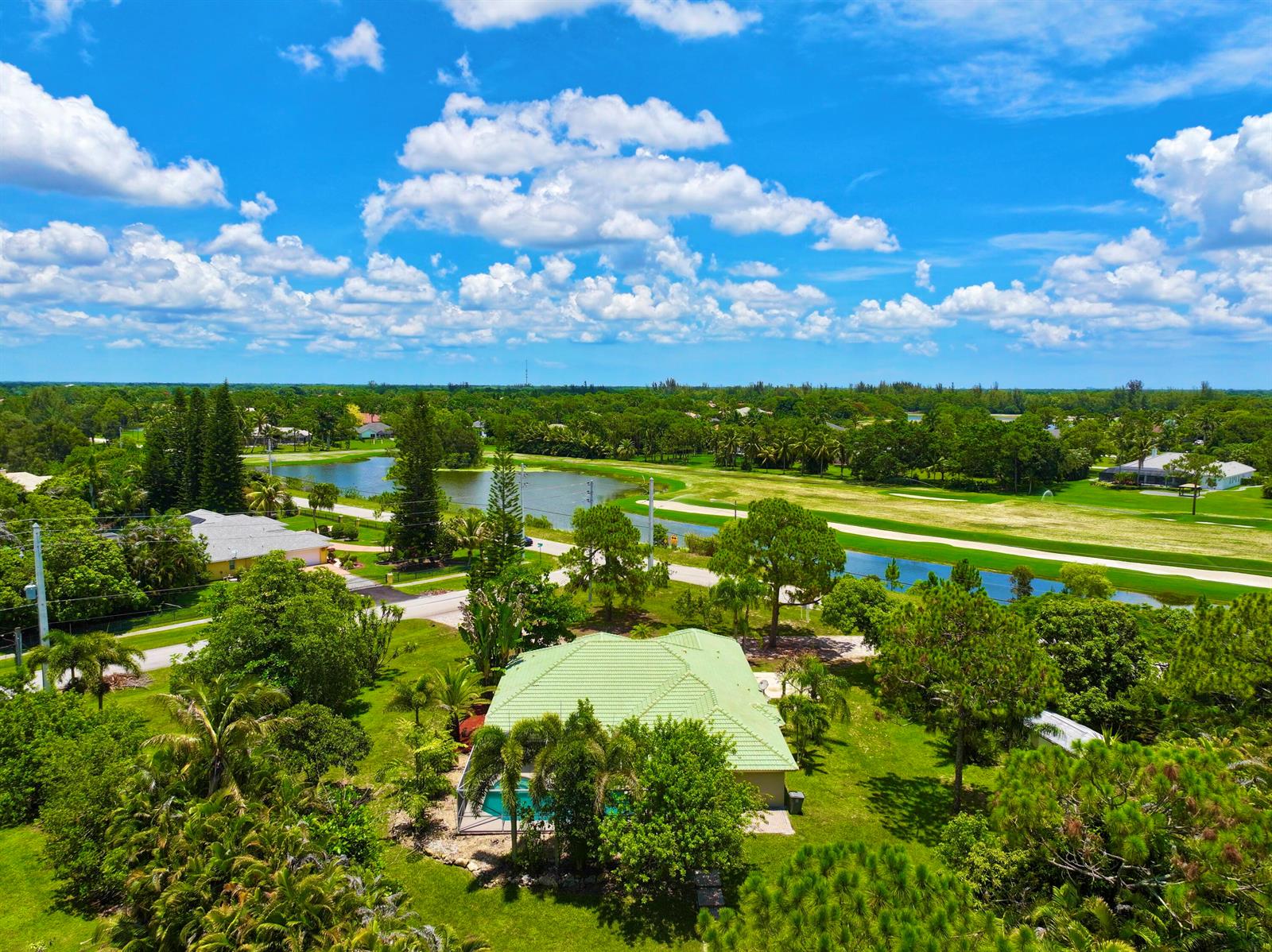 An aerial view shows a house with a green roof, pool, and surrounding landscape — 12037 Temple Boulevard, FL 33412, FL