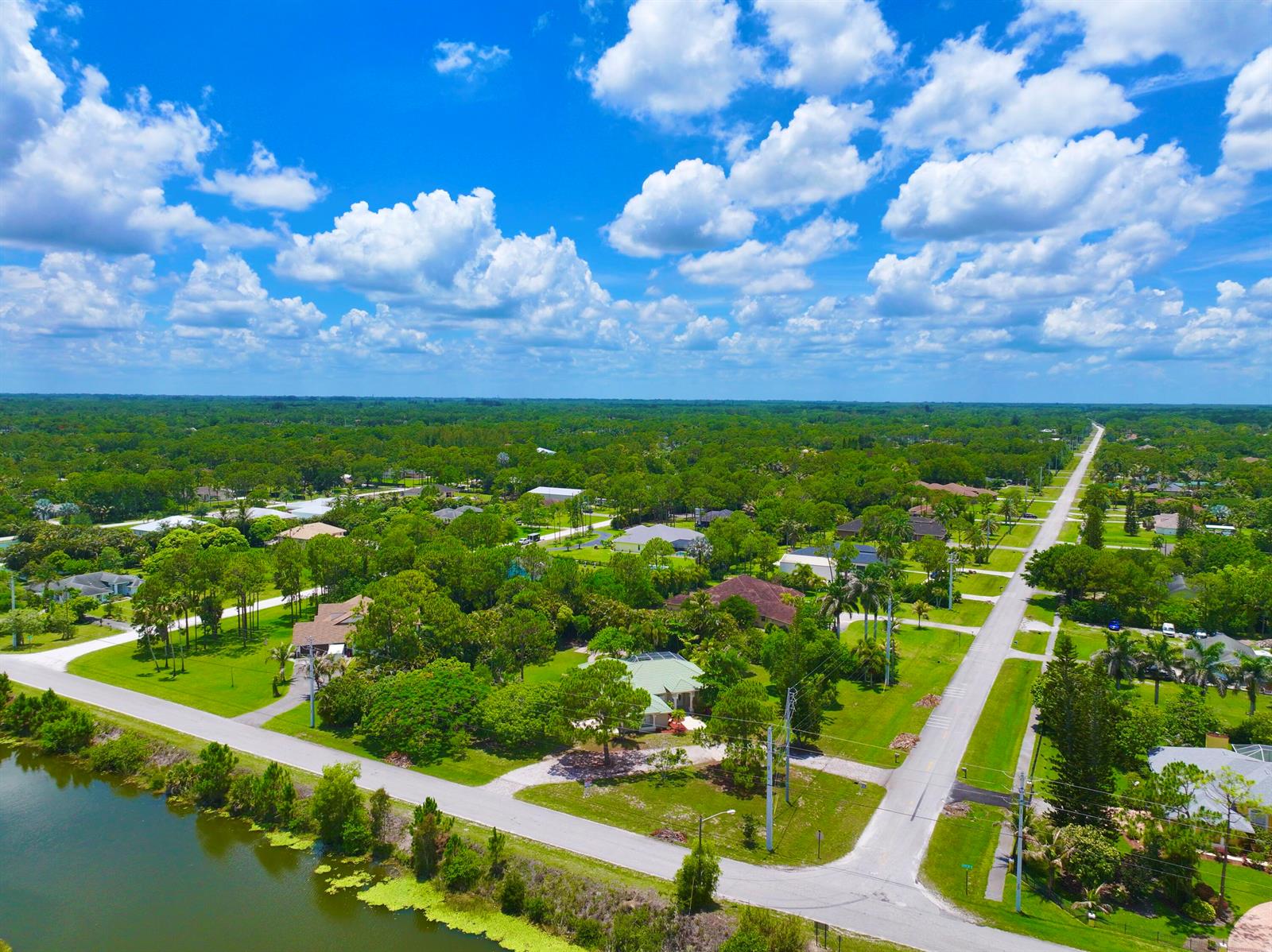 An aerial view shows a suburban neighborhood with houses, green lawns, and a nearby pond — 12037 Temple Boulevard, FL 33412, FL