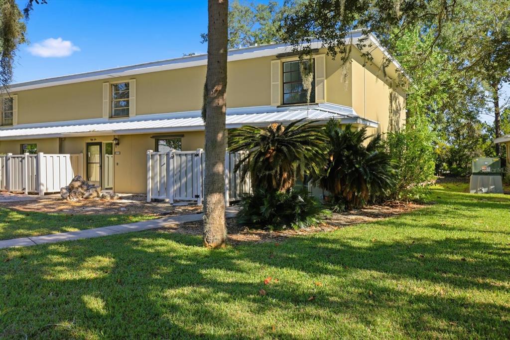 A two-story tan townhouse with a white metal roof and a private fenced patio area — 11328 W BAYSHORE DRIVE, CRYSTAL RIVER, FL