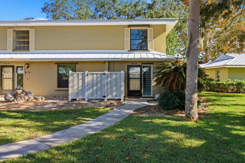 A two-story tan building with a white metal roof, sidewalk, and a small privacy fence — 11328 W BAYSHORE DRIVE, CRYSTAL RIVER, FL