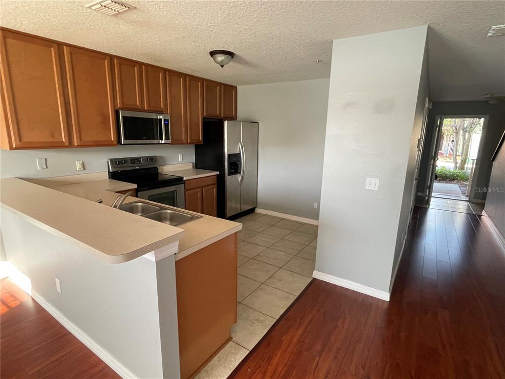 A kitchen features wood cabinets, stainless steel appliances, a breakfast bar, and tile flooring — 13433 STARRY NIGHT COURT UNIT 11, ORLANDO, FL