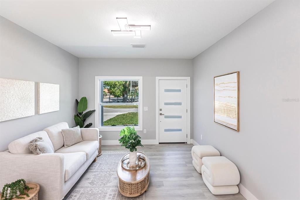 A bright living room features a white sofa, oval coffee table, and a modern front door — 1024 SENTINELA BOULEVARD, LEHIGH ACRES, FL